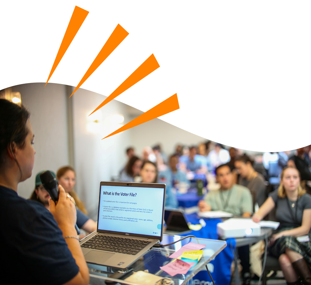 A person training a group of people taking notes. The slide visible on their laptop shows "What is the Voter File?"